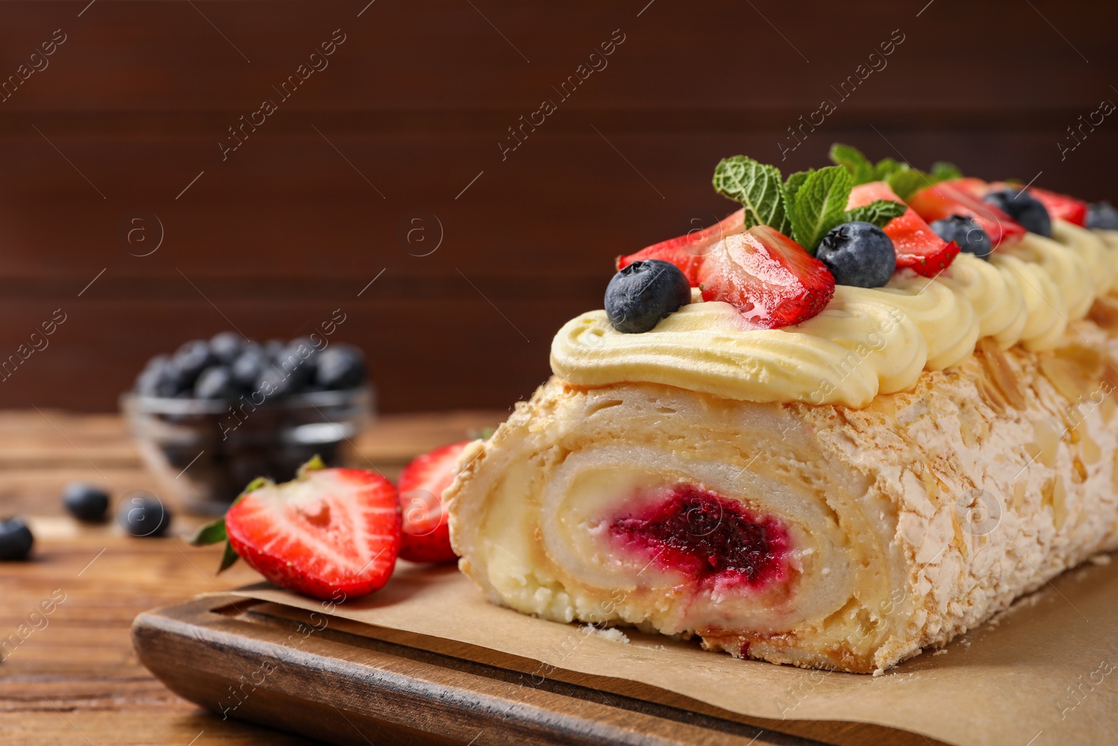Photo of Tasty meringue roll with jam, cream, strawberry, blueberry and mint on wooden table, closeup