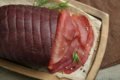 Photo of Tasty bresaola, peppercorns and rosemary on wooden table, top view