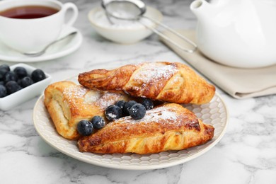 Photo of Fresh tasty puff pastry with sugar powder and blueberries served on white marble table, closeup