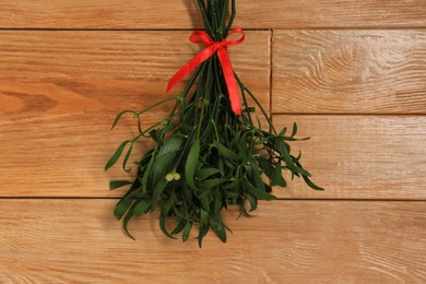Photo of Mistletoe bunch with red bow on wooden table, top view. Traditional Christmas decor