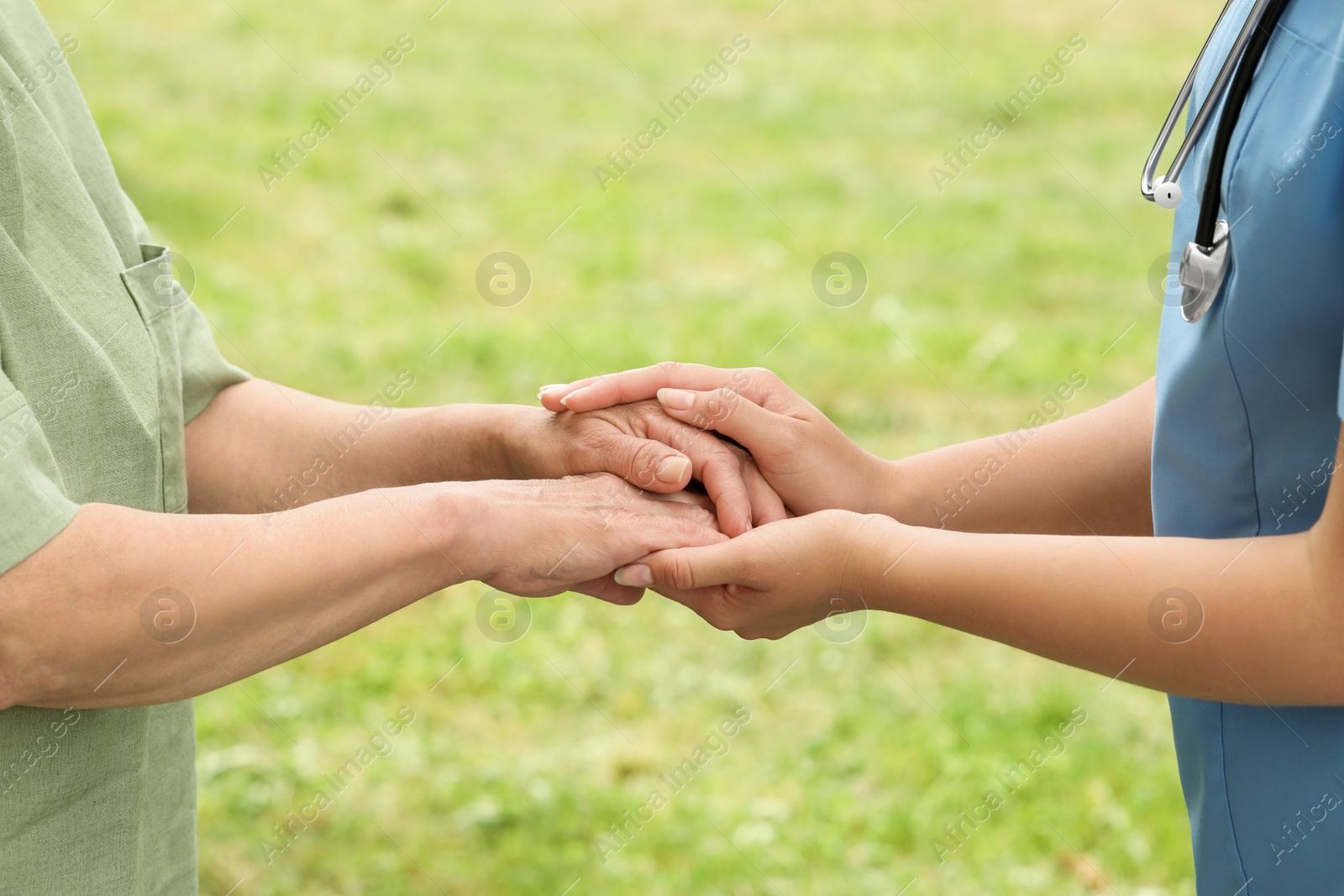 Photo of Elderly woman and female caregiver holding hands outdoors, closeup