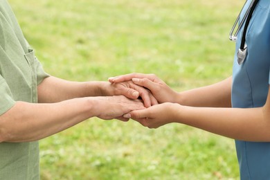 Photo of Elderly woman and female caregiver holding hands outdoors, closeup