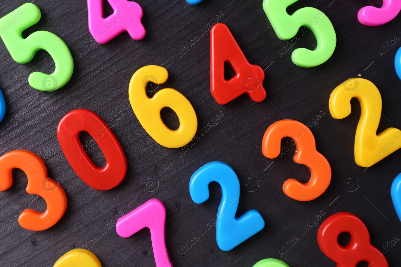 Photo of Colorful numbers on dark wooden school desk, flat lay