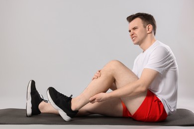 Photo of Man suffering from leg pain on mat against grey background