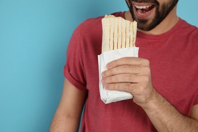 Photo of Young man eating tasty shawarma on turquoise background, closeup