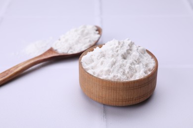 Photo of Wooden bowl and spoon of natural starch on white tiled table, closeup