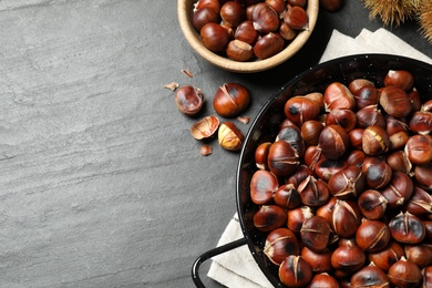 Photo of Delicious roasted edible chestnuts on black slate table, flat lay. Space for text