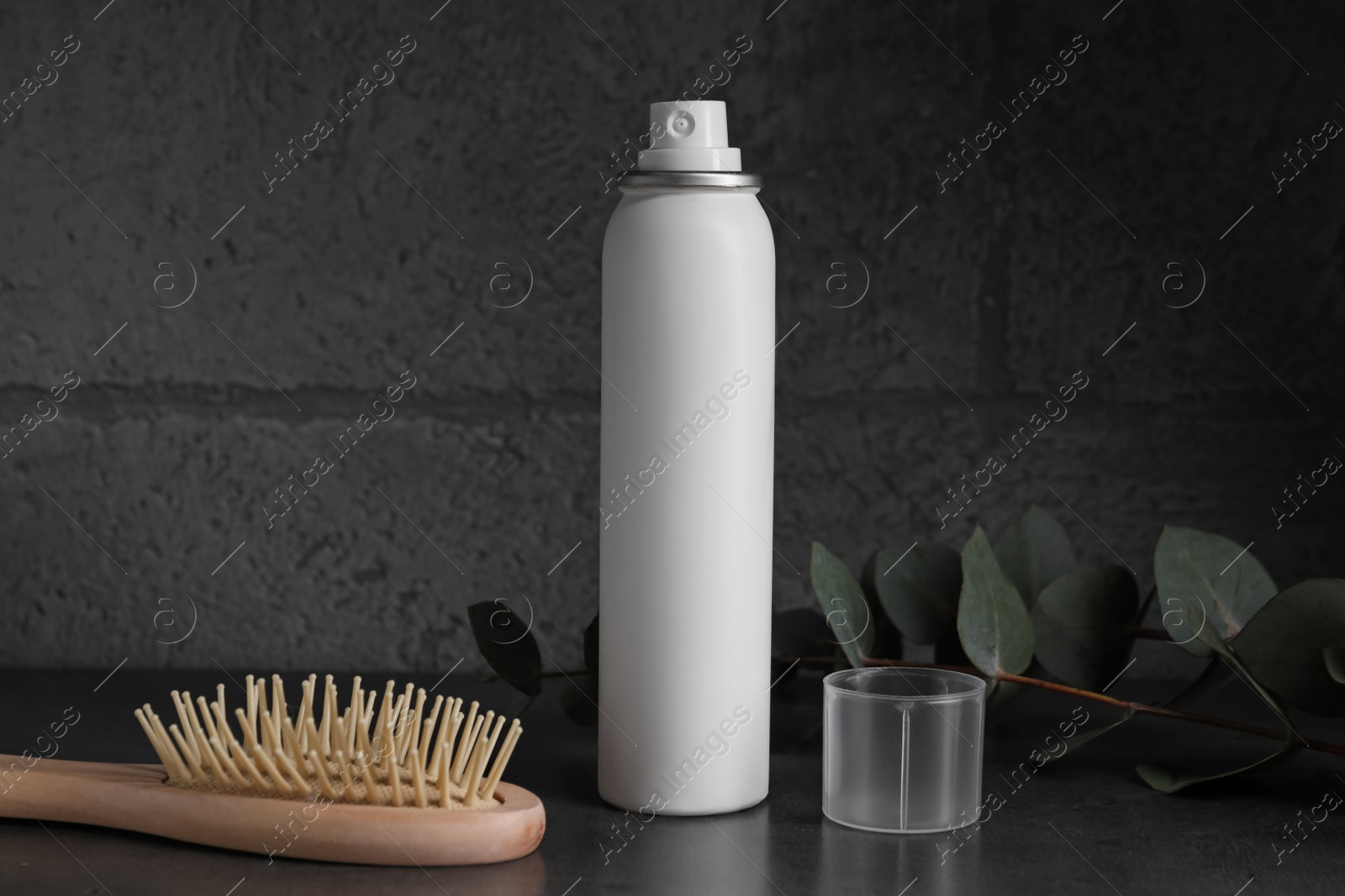 Photo of Dry shampoo spray, eucalyptus branch and hairbrush on dark table near grey wall