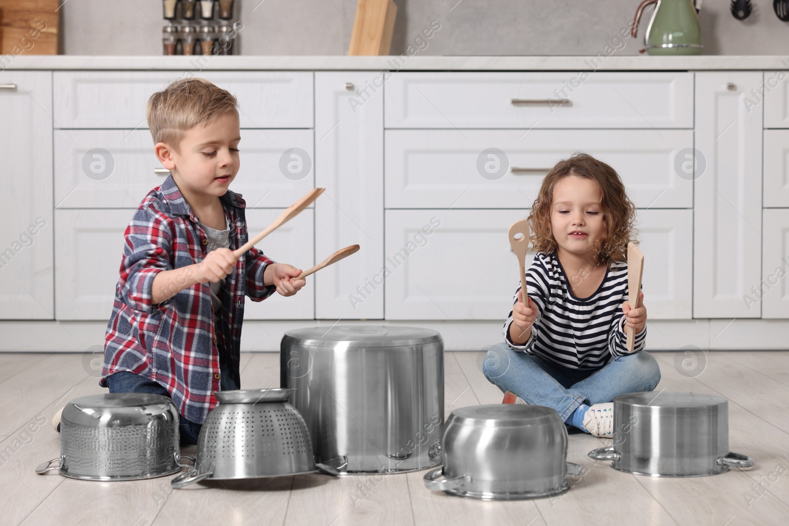 Photo of Little children pretending to play drums on pots in kitchen