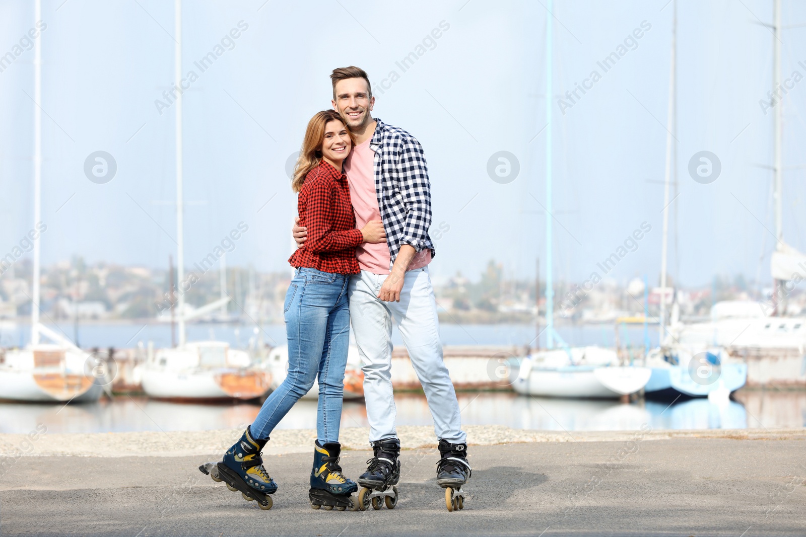 Photo of Happy lovely couple roller skating on embankment. Space for text