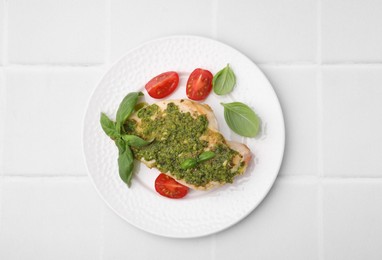 Photo of Delicious chicken breast with pesto sauce, tomatoes and basil on white tiled table, top view