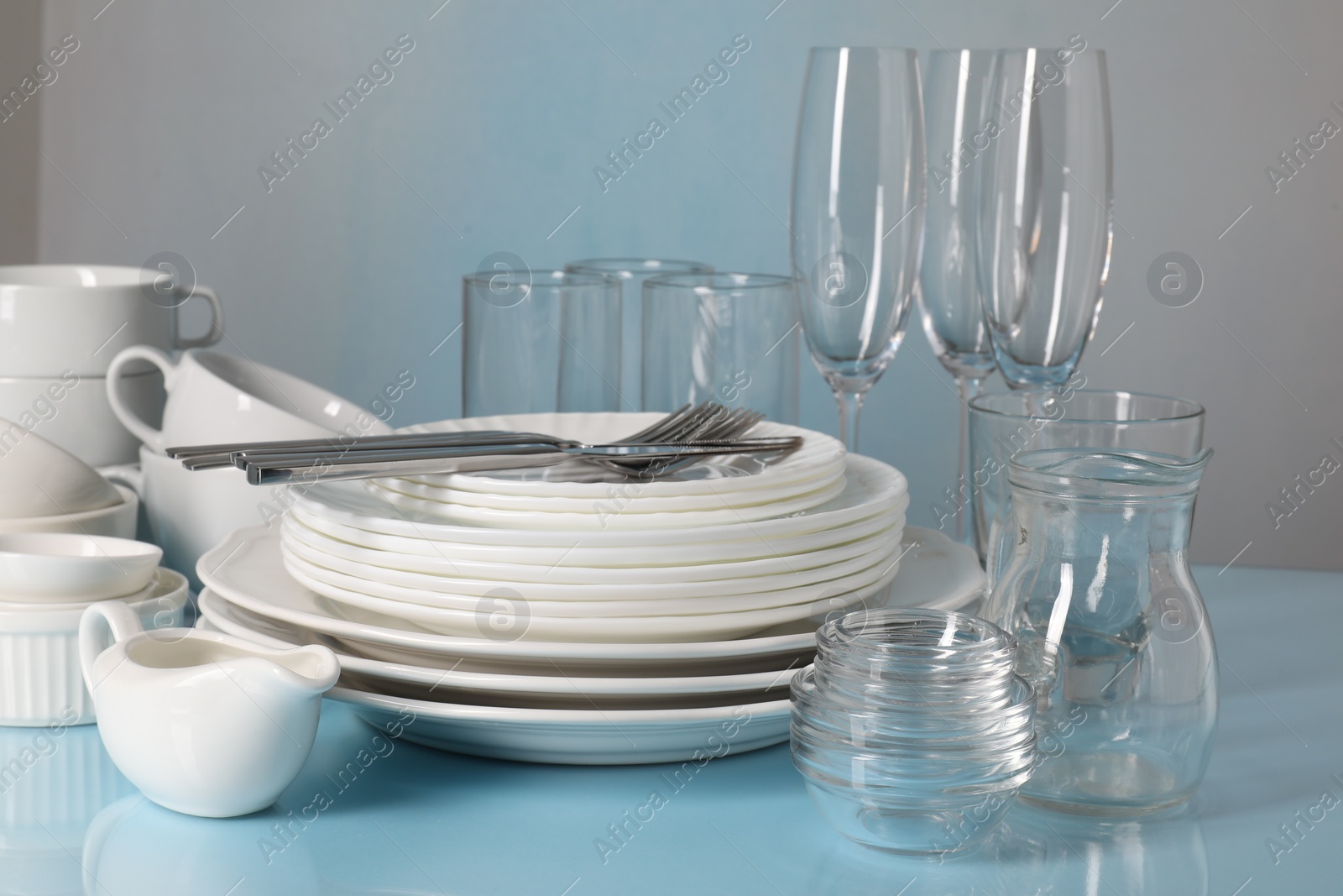 Photo of Set of clean dishes, glasses and cutlery on light blue table