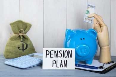 Photo of Card with phrase Pension Plan, mannequin hand holding dollar banknote, piggy bank, sack and calculator on light blue wooden table. Retirement concept