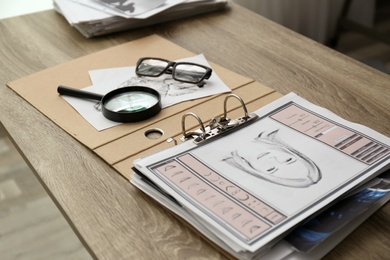 Papers with suspect's portrait, palm print and magnifying glass on wooden table in detective office