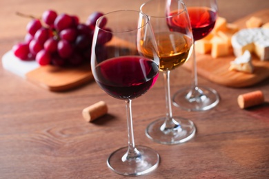 Photo of Glasses with different wines and appetizers on wooden table
