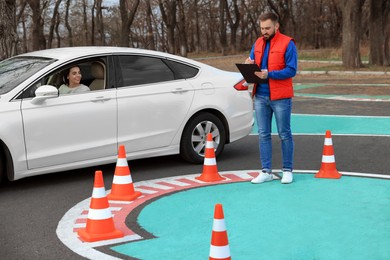 Instructor near car with his student during exam at driving school test track