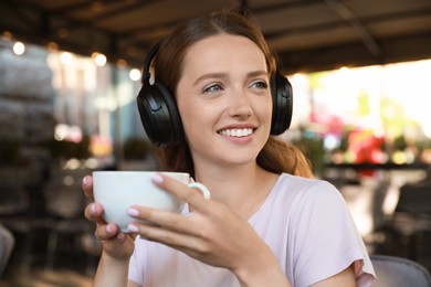 Photo of Smiling woman in headphones drinking coffee outdoors