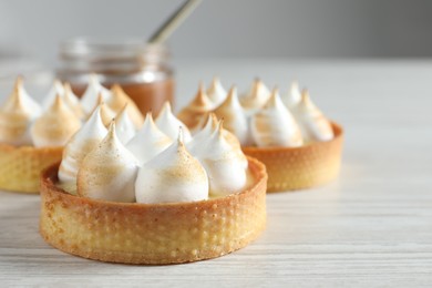 Photo of Tasty dessert. Tartlets with meringue on white wooden table, closeup. Space for text
