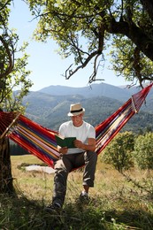 Photo of Handsome man reading book in hammock outdoors on sunny day