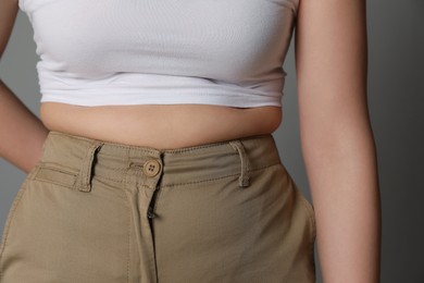 Overweight woman in tight pants on grey background, closeup
