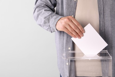 Man putting his vote into ballot box on light grey background, closeup. Space for text