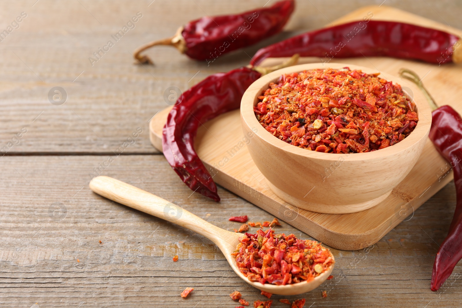 Photo of Aromatic spice. Red chili pepper flakes in bowl, spoon and pods on wooden table, closeup. Space for text