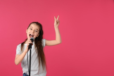 Photo of Cute girl singing in microphone on color background. Space for text