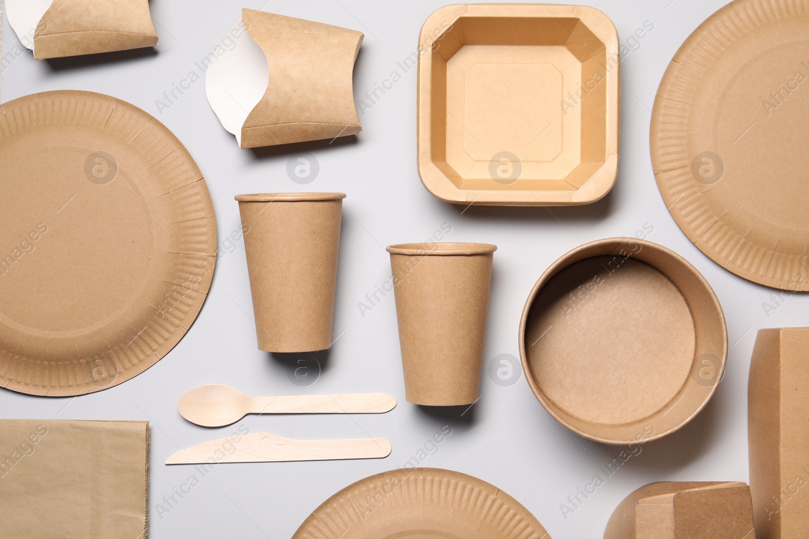 Photo of Eco friendly food packaging. Paper containers and tableware on light grey background, flat lay