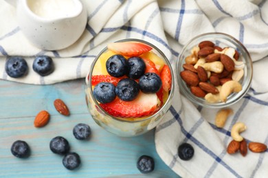 Photo of Delicious fruit salad, fresh berries and nuts on light blue wooden table, flat lay