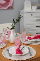 Photo of Color accent table setting. Glasses, plates, vase with green branch and pink napkins in dining room