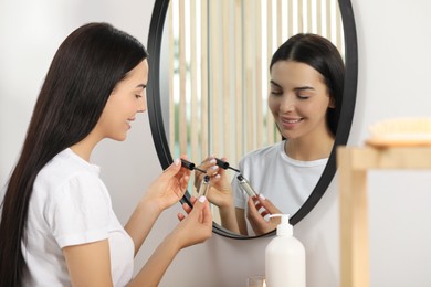 Young woman with eyelash oil near mirror indoors