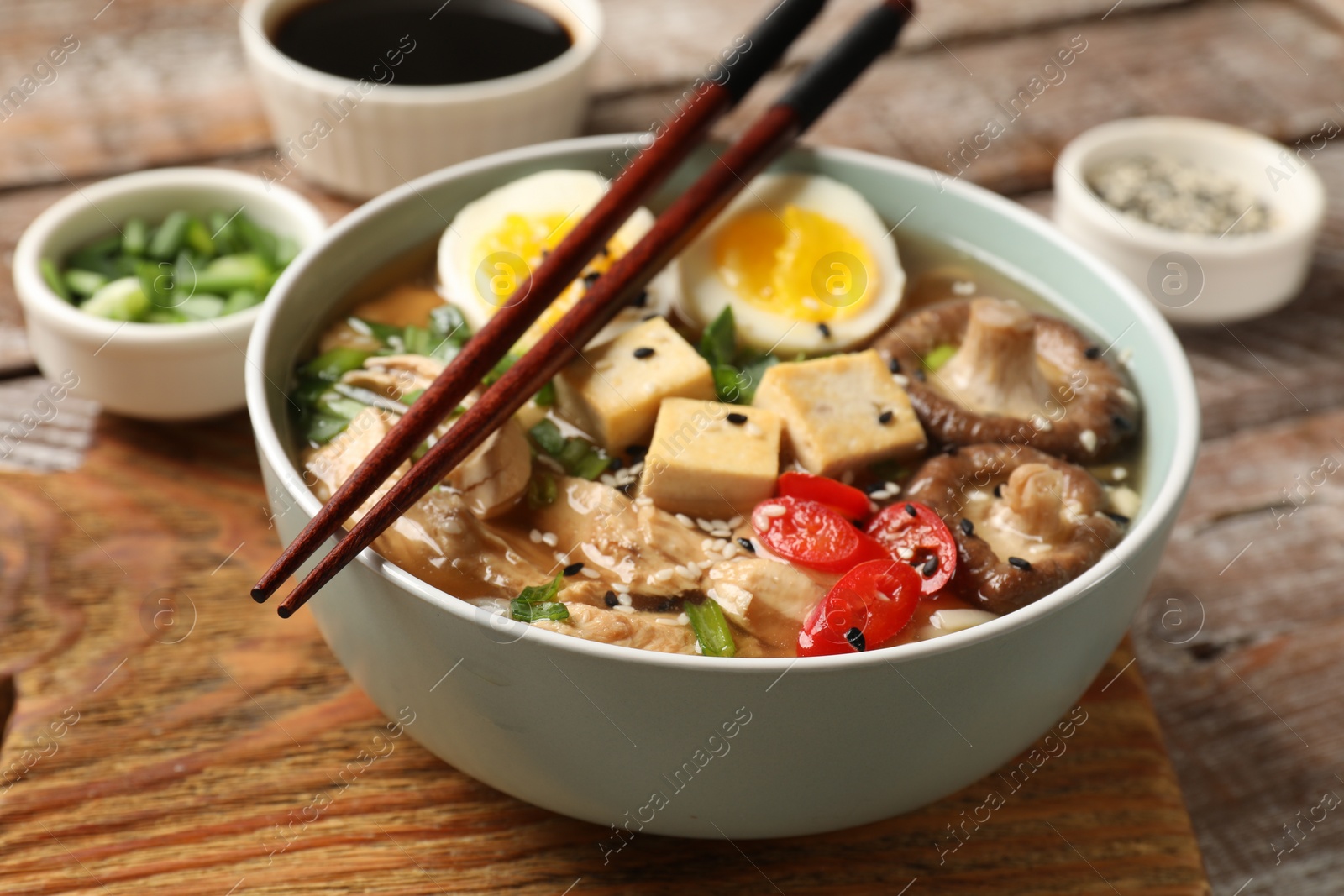 Photo of Noodle soup. Bowl of delicious ramen and chopsticks on wooden table, closeup