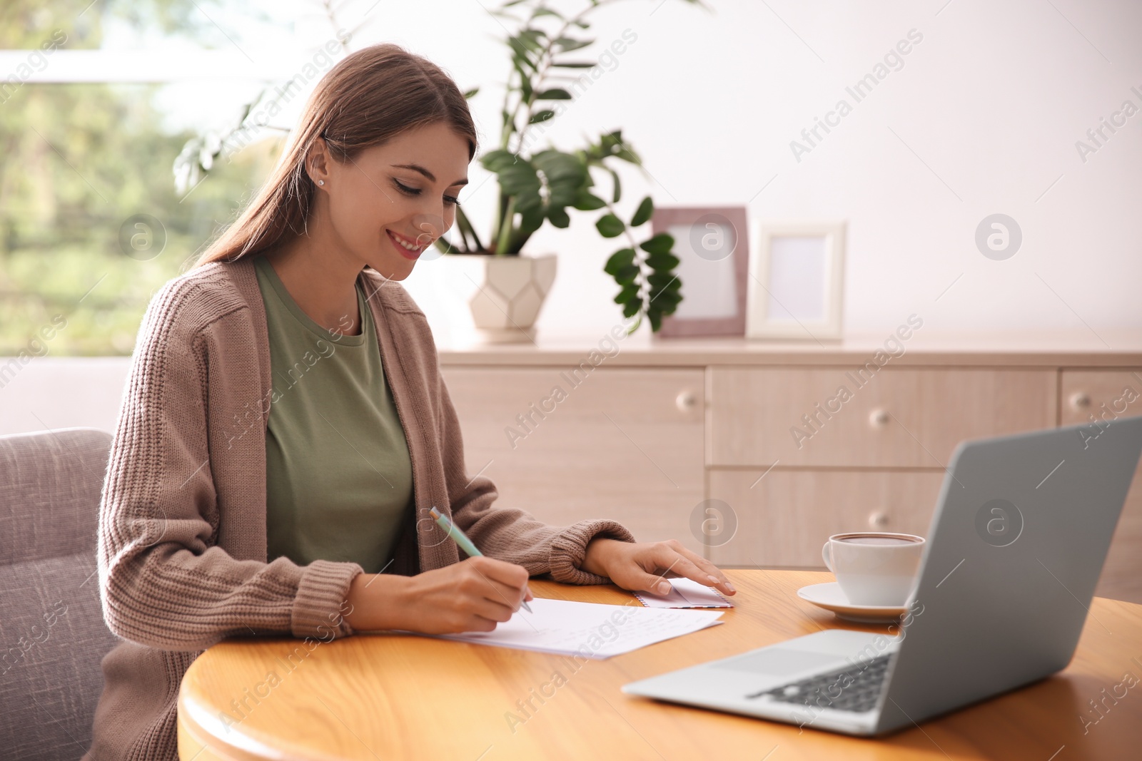 Photo of Woman writing letter at wooden table in room