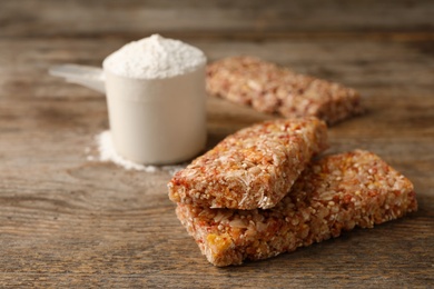 Photo of Tasty protein bars and scoop of powder on wooden table. Space for text