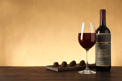 Photo of Bottle and glass of red wine with chocolate candies on wooden table. Space for text