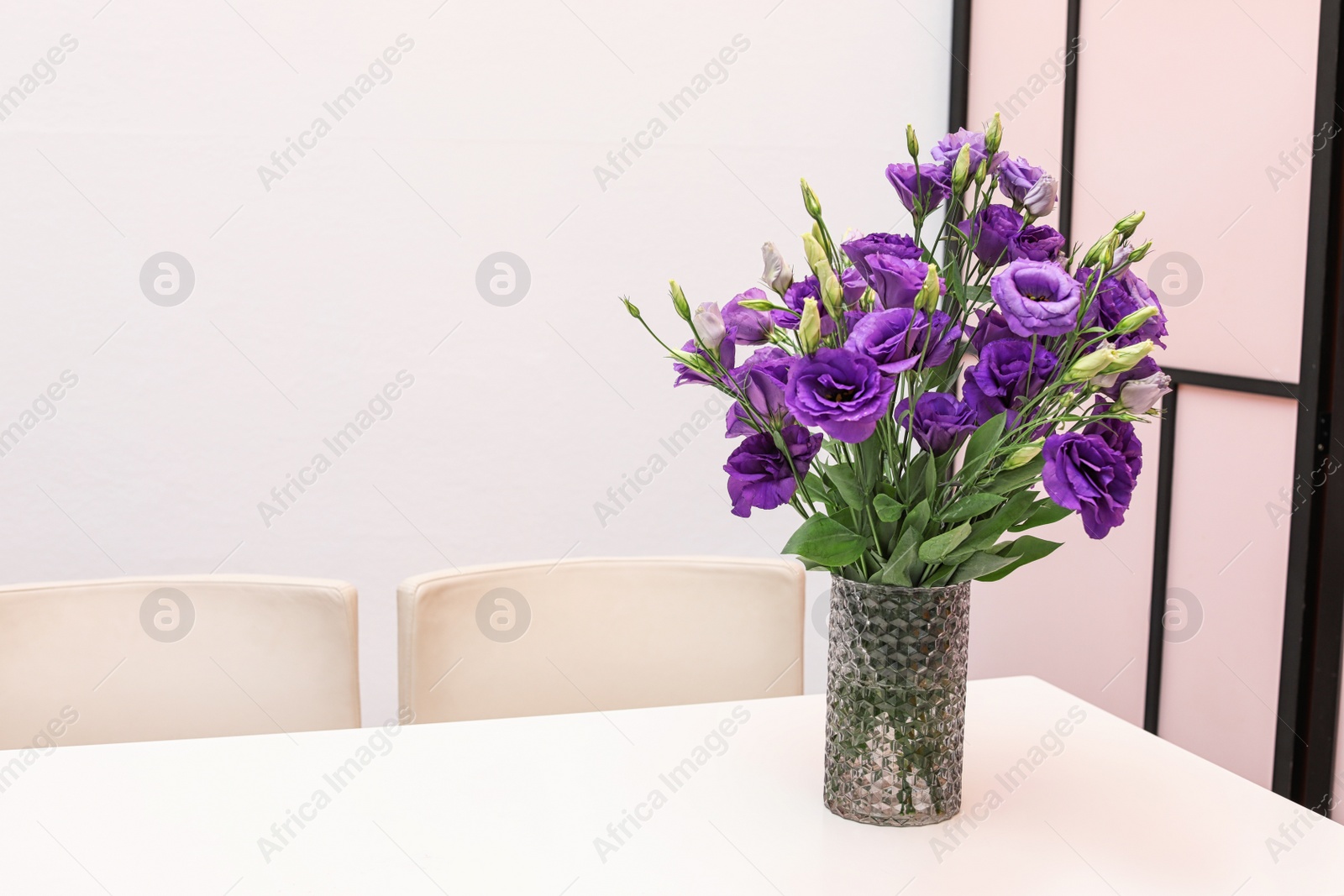 Photo of Vase with beautiful flowers on white table against color background. Stylish interior