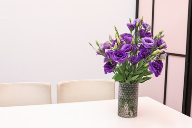 Photo of Vase with beautiful flowers on white table against color background. Stylish interior