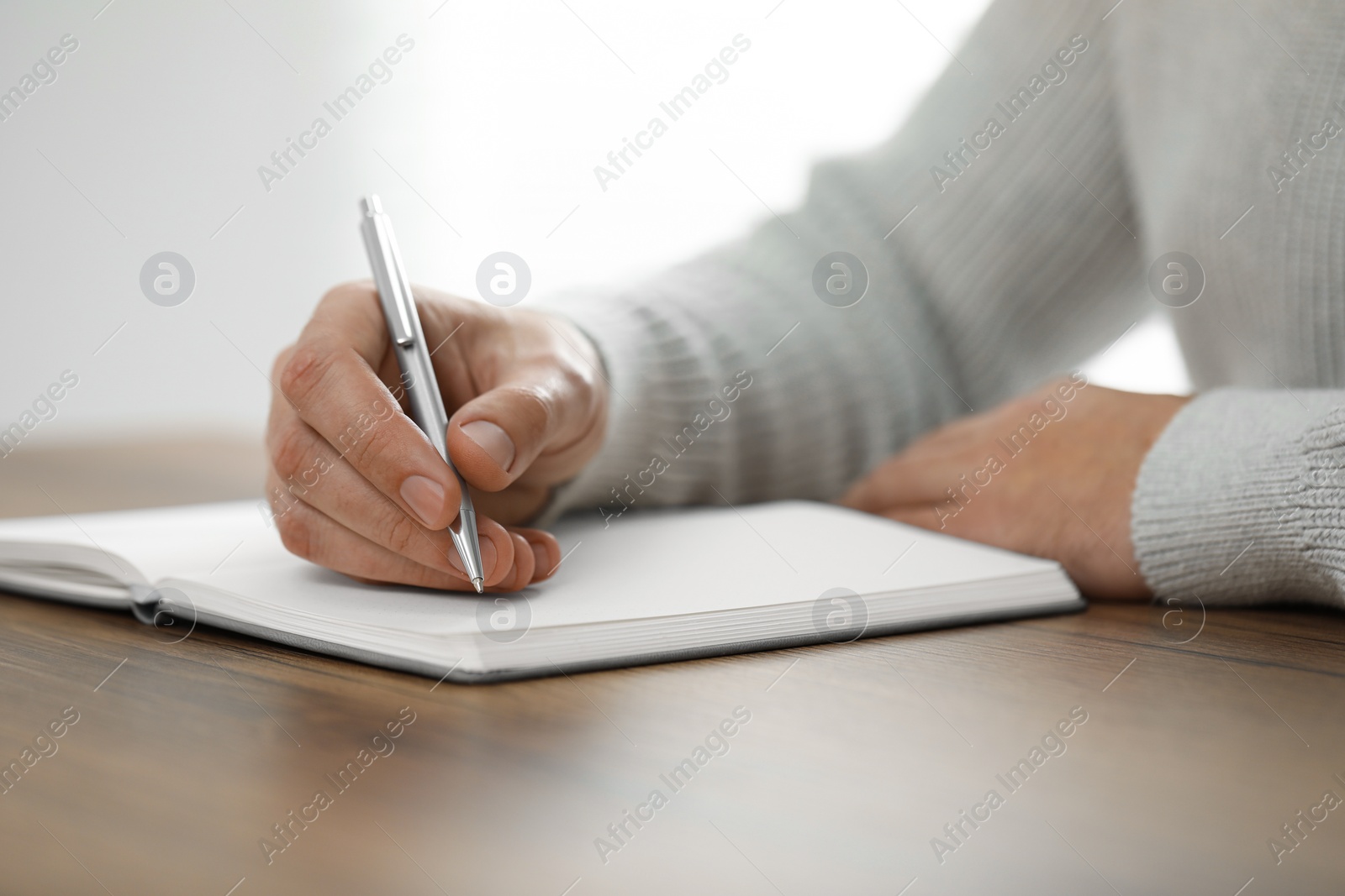 Photo of Man writing in notebook at wooden table, closeup