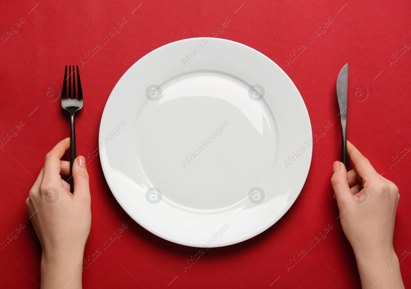 Photo of Woman with empty plate and cutlery on red background, top view