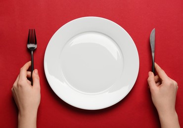 Woman with empty plate and cutlery on red background, top view