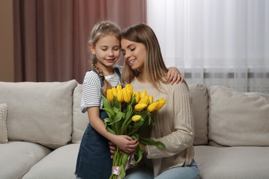 Photo of Little daughter congratulating mom with bouquet of yellow tulips at home. Happy Mother's Day