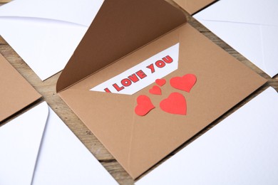 Photo of Sheet of paper with phrase I Love You, envelopes and red hearts on wooden table, closeup