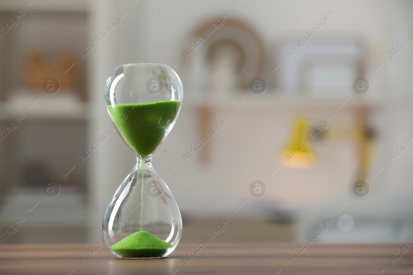 Photo of Hourglass with light green flowing sand on table against blurred background. Space for text