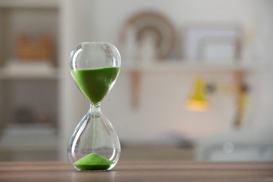 Photo of Hourglass with light green flowing sand on table against blurred background. Space for text