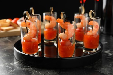 Photo of Tasty canapes with shrimps, tomatoes and sauce in shot glasses on black marble table, closeup