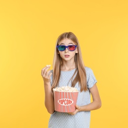 Emotional teenage girl with 3D glasses and popcorn during cinema show on color background