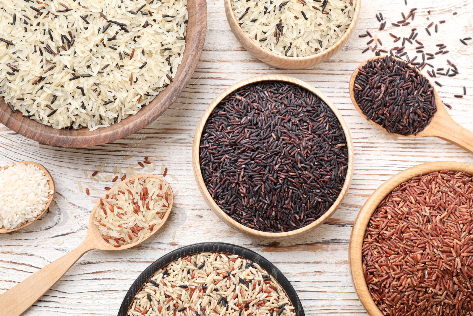 Photo of Different sorts of rice on white wooden table, flat lay