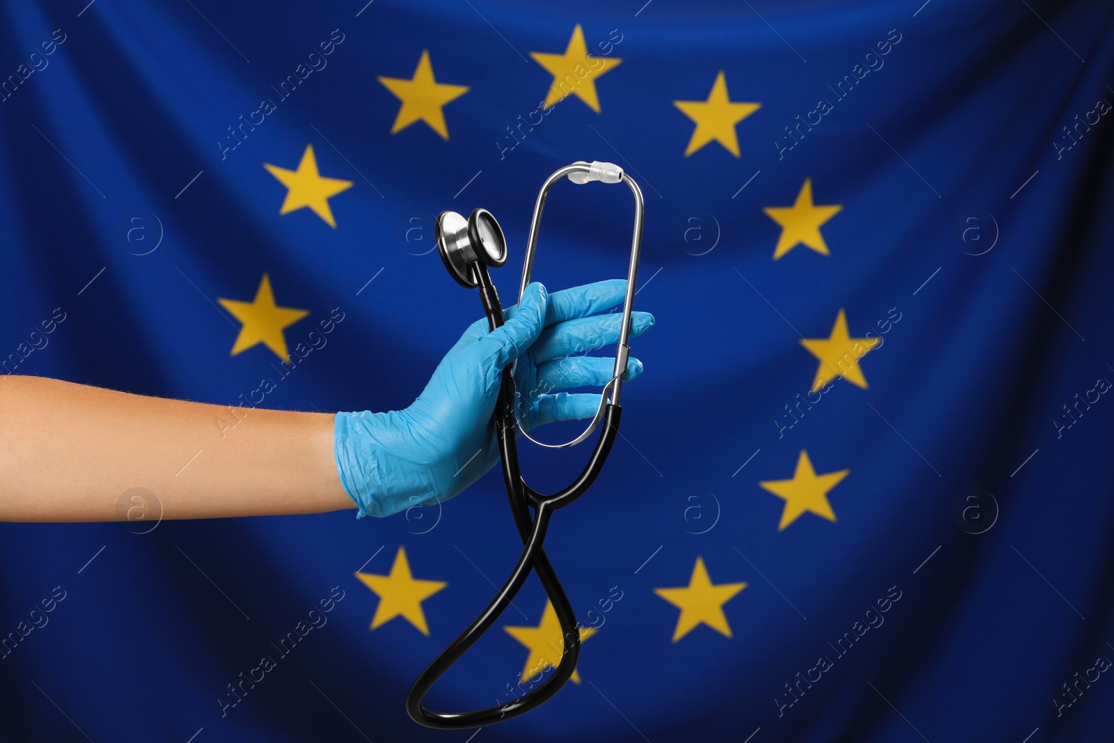 Photo of Woman holding stethoscope against flag of European Union, closeup