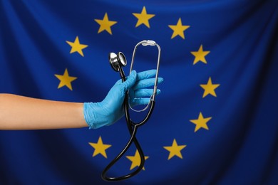 Photo of Woman holding stethoscope against flag of European Union, closeup