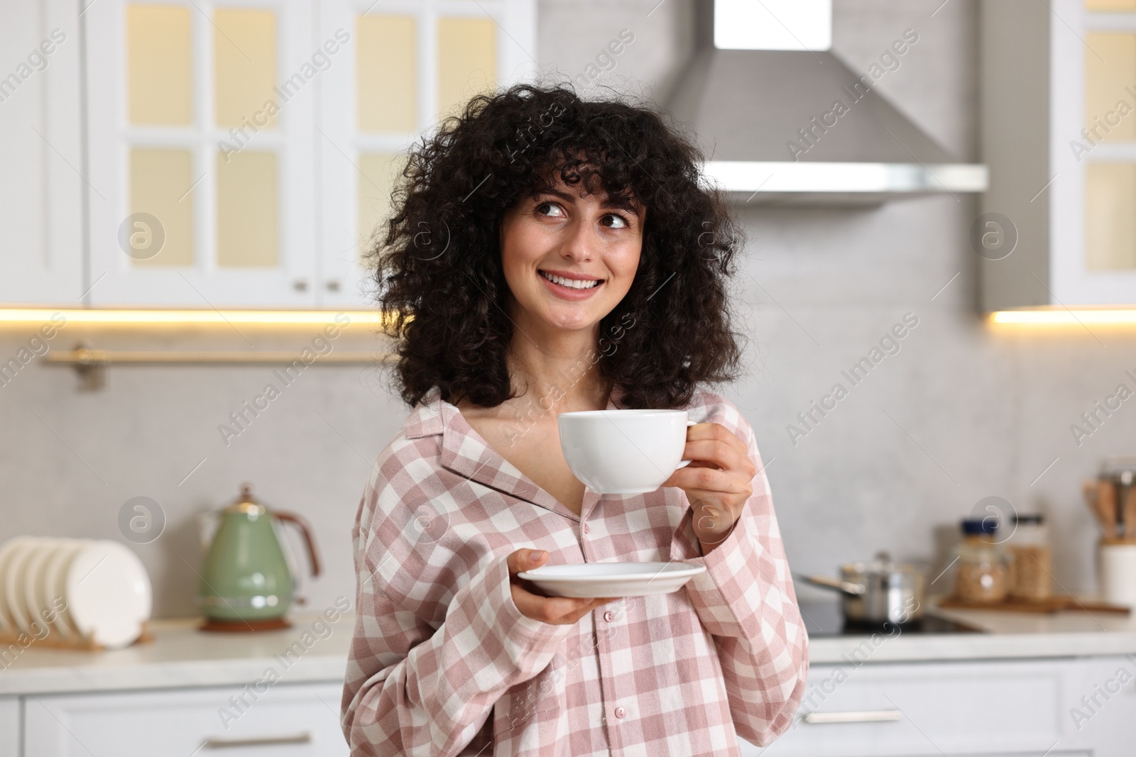 Photo of Beautiful young woman in stylish pyjama with cup of drink in kitchen